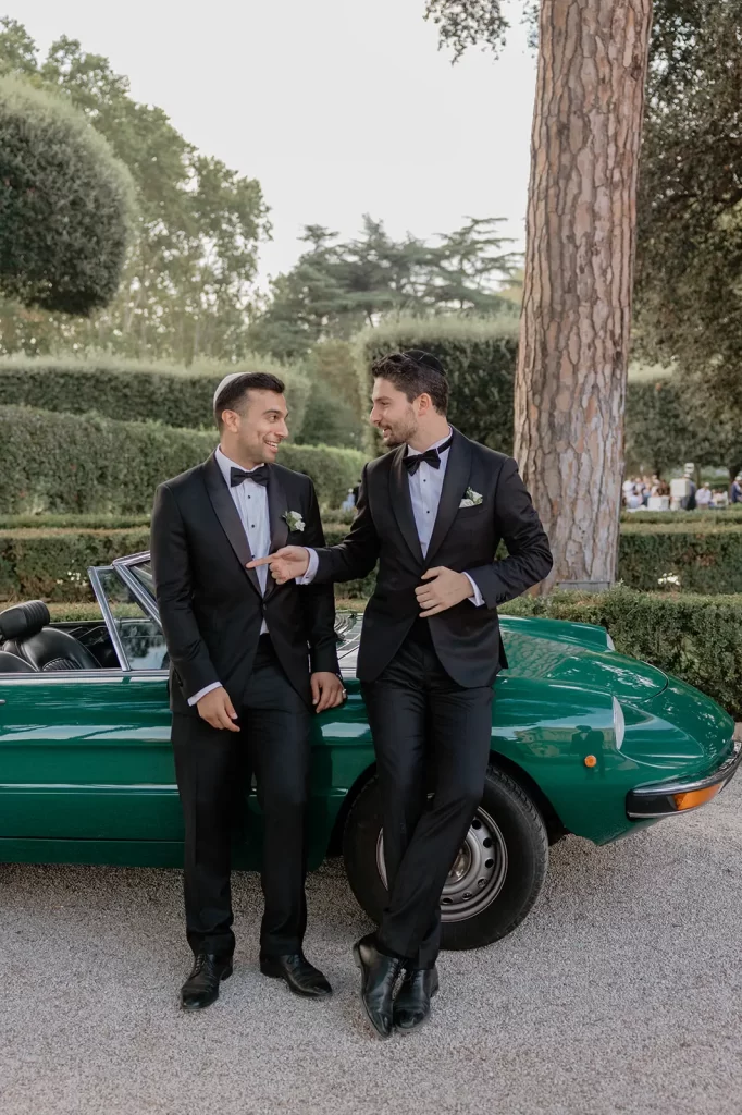 two men are leaning against a vintage green car