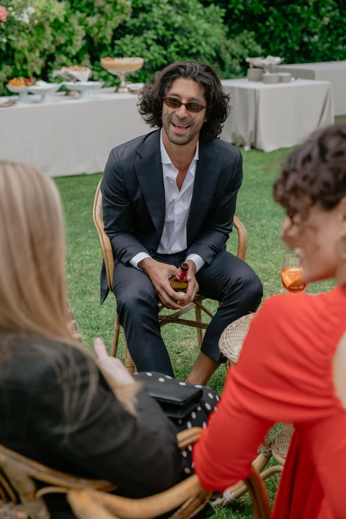 a man is laughing sitting on a chair while he is talking with 2 girls