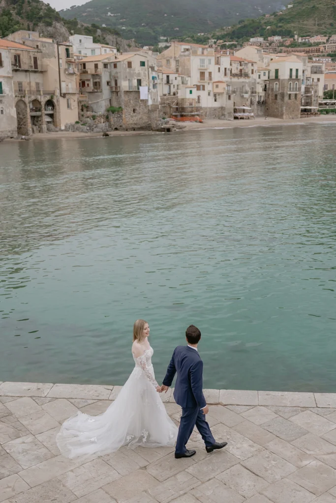 newlywed couple is walking along the Porticciolo in Cefalù, Sicily