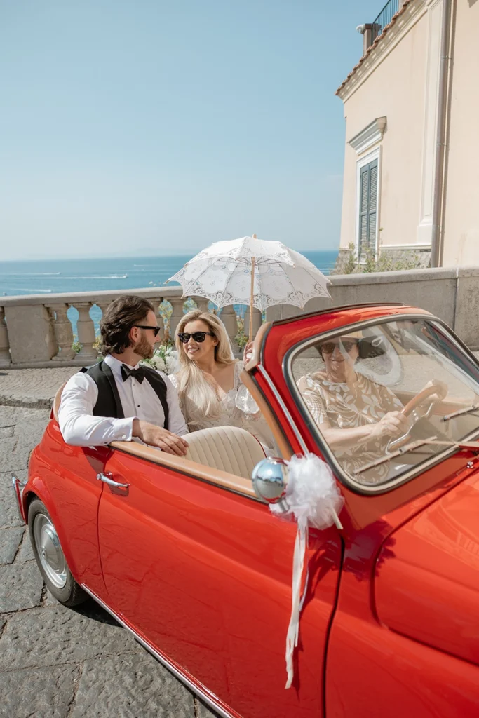 newlywed couple in a red cinquecento car with sea in the background