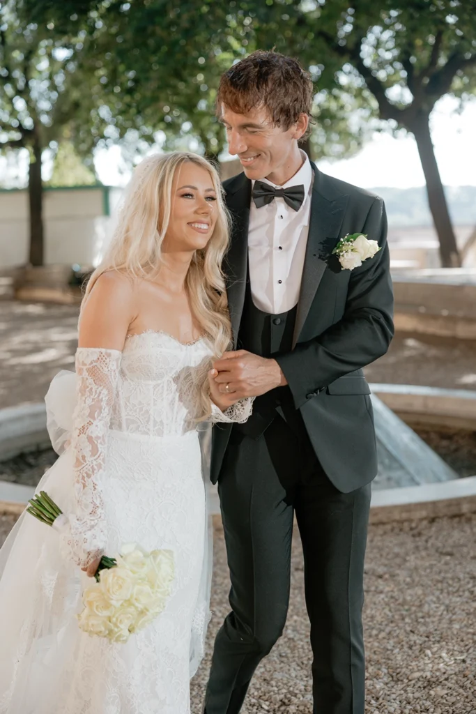 a newlywed couple is walking and smiling in a garden