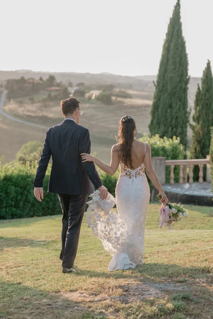 a newlywed couple is walking against tuscan landscape