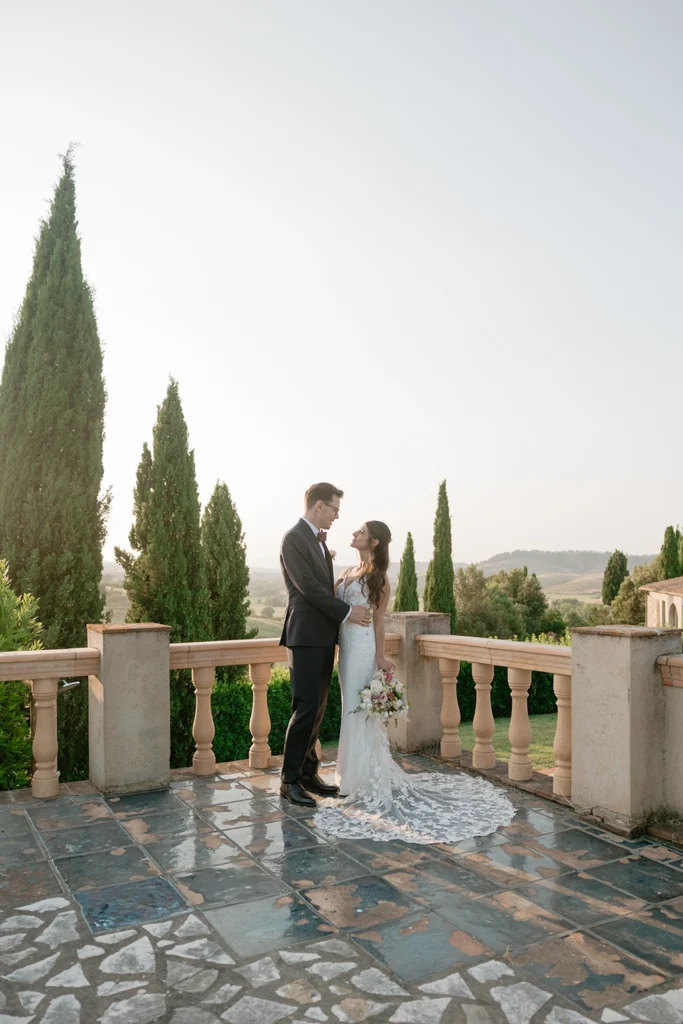 a newlywed couple is standing against tuscan landscape