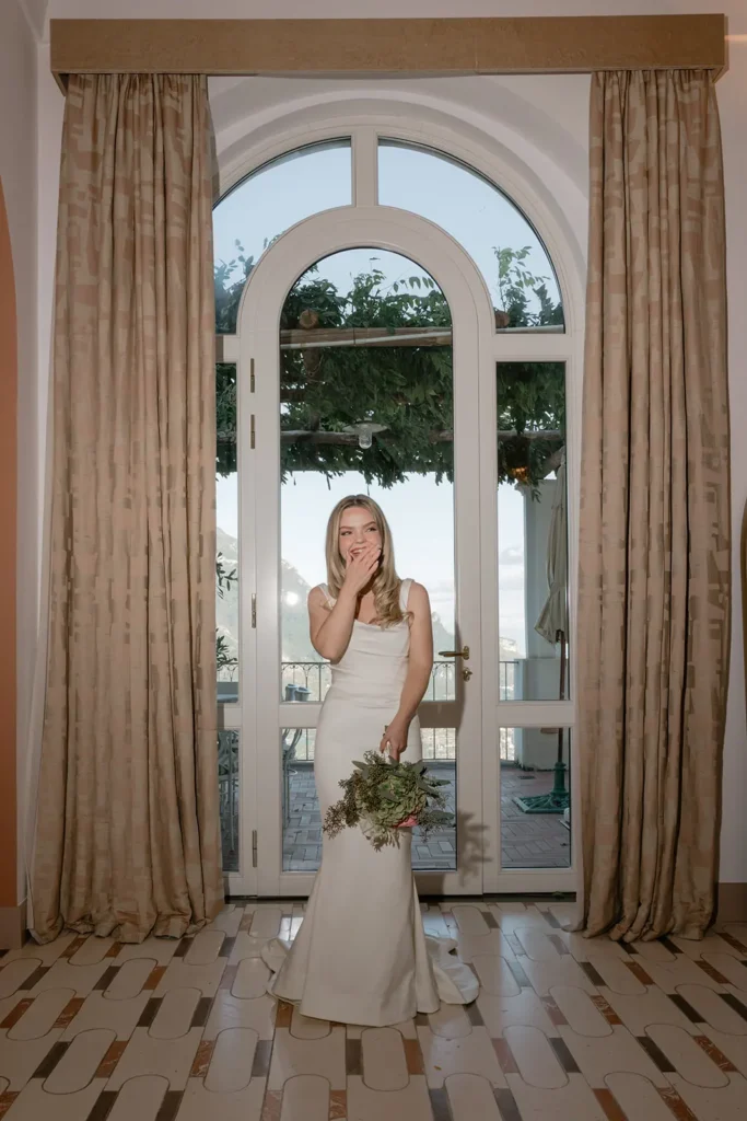bride is smiling in front of a tall window