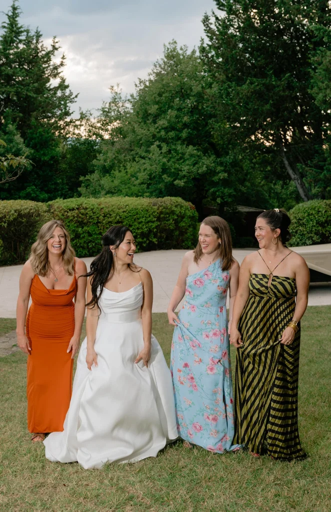 3 girls and a bride are walking in a garden and smiling at each other
