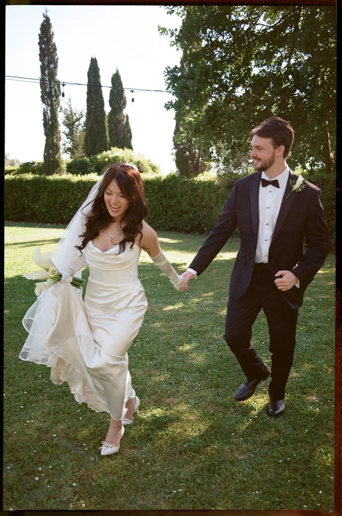 a bride and a groom are smiling and running in a garden